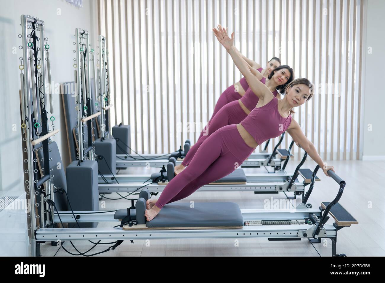 Three Asian women in pink sportswear doing side planks on a reformer.  Pilates classes Stock Photo - Alamy