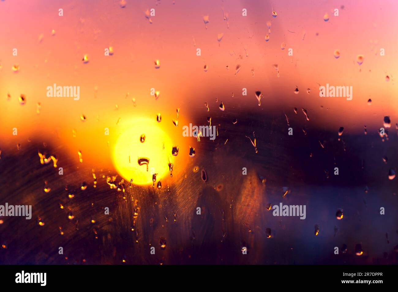 Blurred background of water droplets on a dirty glass window at sunset. Look out the dirty window. Close up wet and dirty glass texture. Stock Photo
