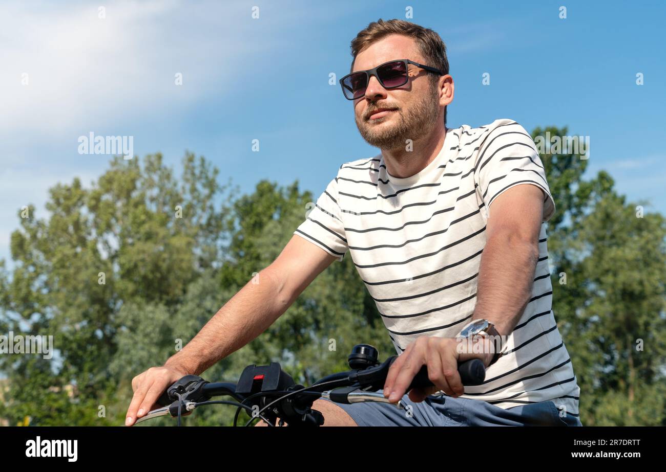 Adult man wearing sunglasses riding a bicycle in the park at the weekend. Stock Photo
