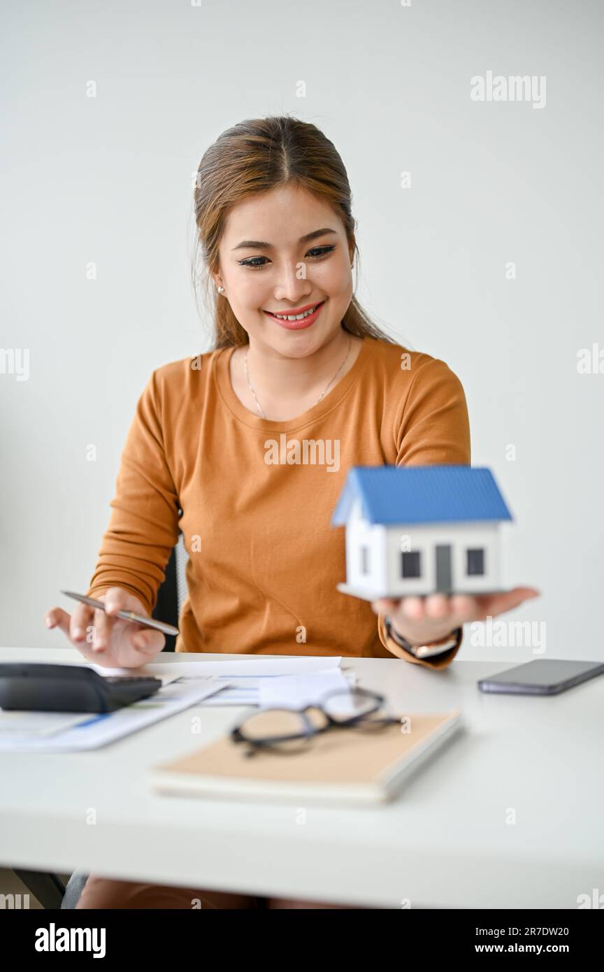 A portrait of a beautiful millennial Asian female real estate agent holding and looking at a