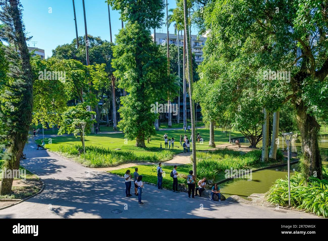 Rio de Janeiro, Brazil - June 8, 2023: People stand on a walkway in a public garden, alongside a flowing water channel. Trees and other individuals ar Stock Photo