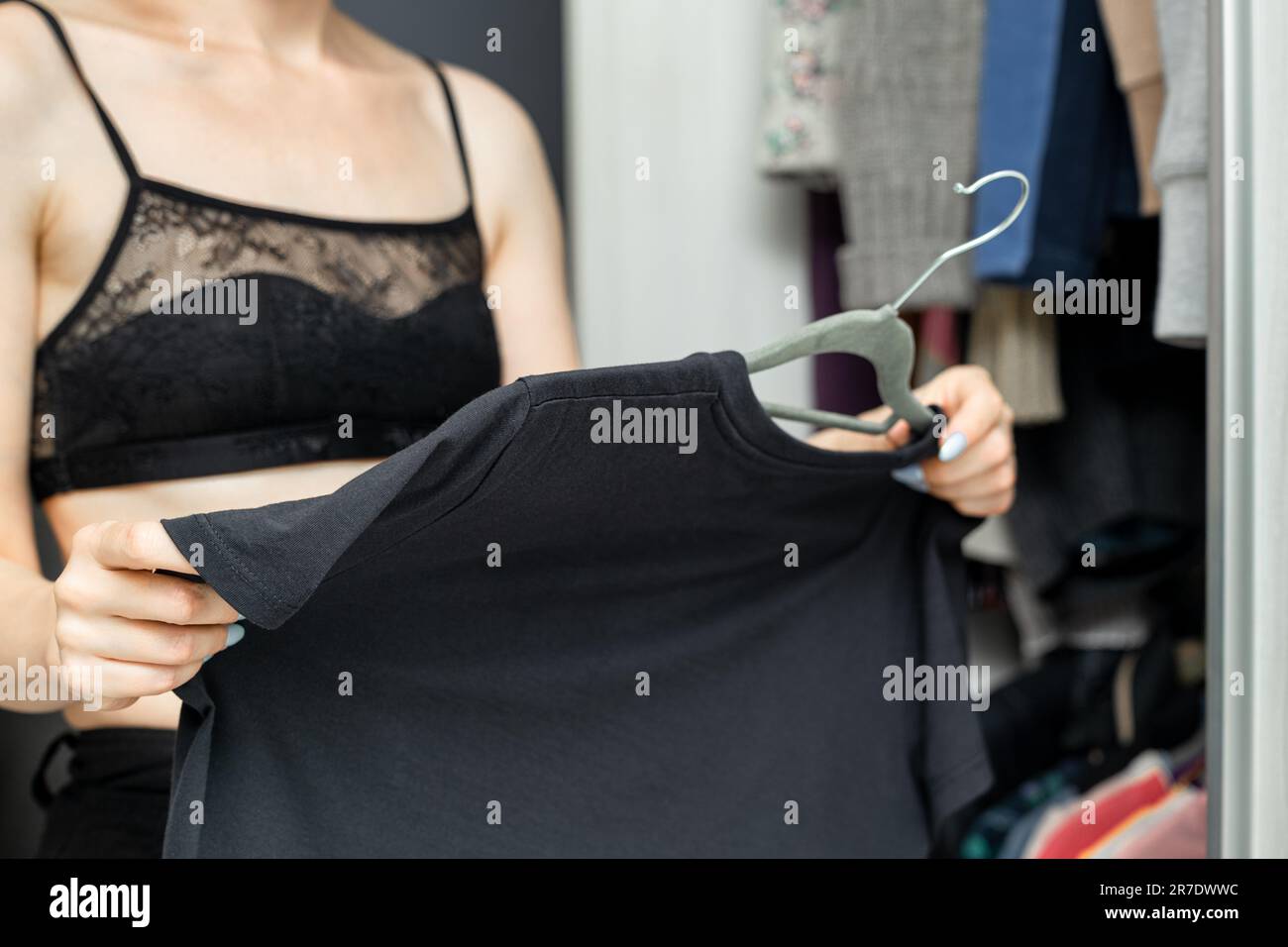 The girl takes off her T-shirt from the hanger. girl decides what to wear Stock Photo