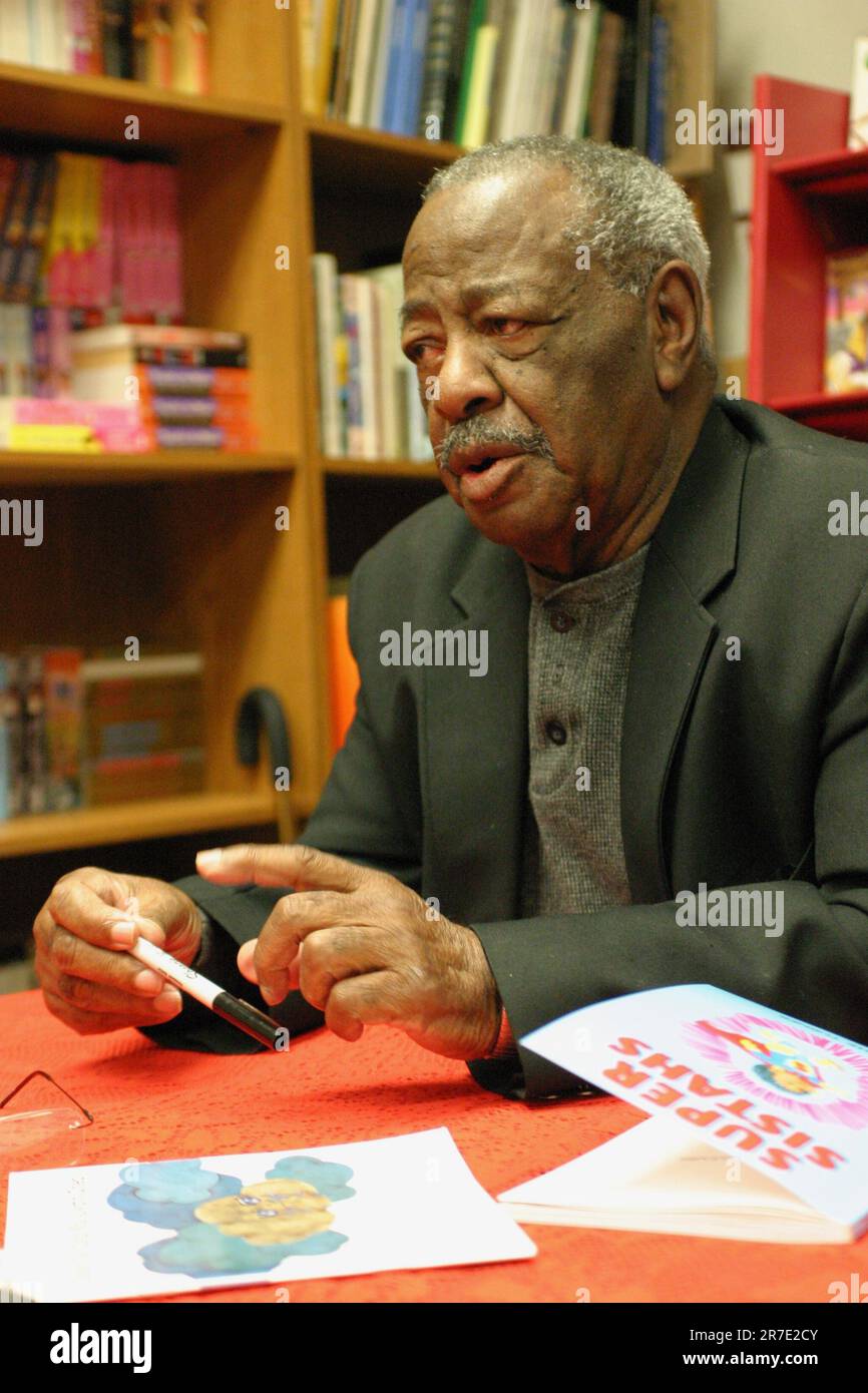 A young man sitting at a desk, looking at a smartphone while reading Stock Photo