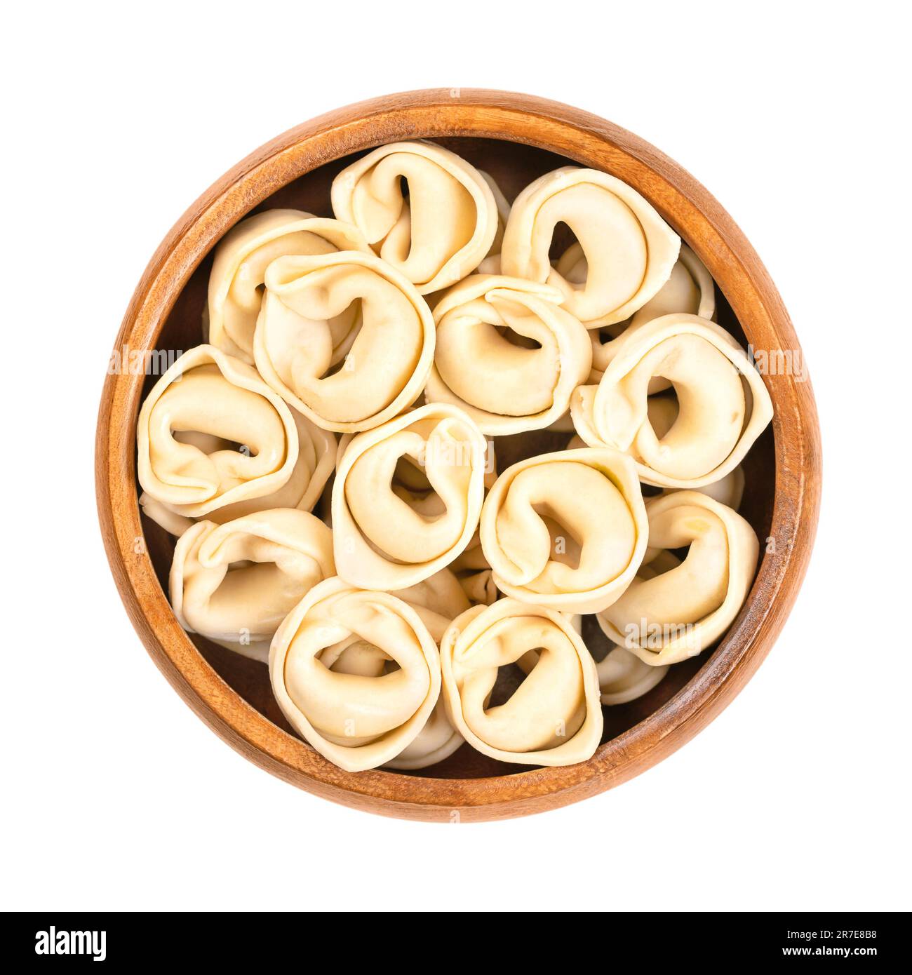 Uncooked, dried tortellini, in a wooden bowl. Industrially made stuffed dumplings, Italian pasta, with distinctive shape. Stock Photo