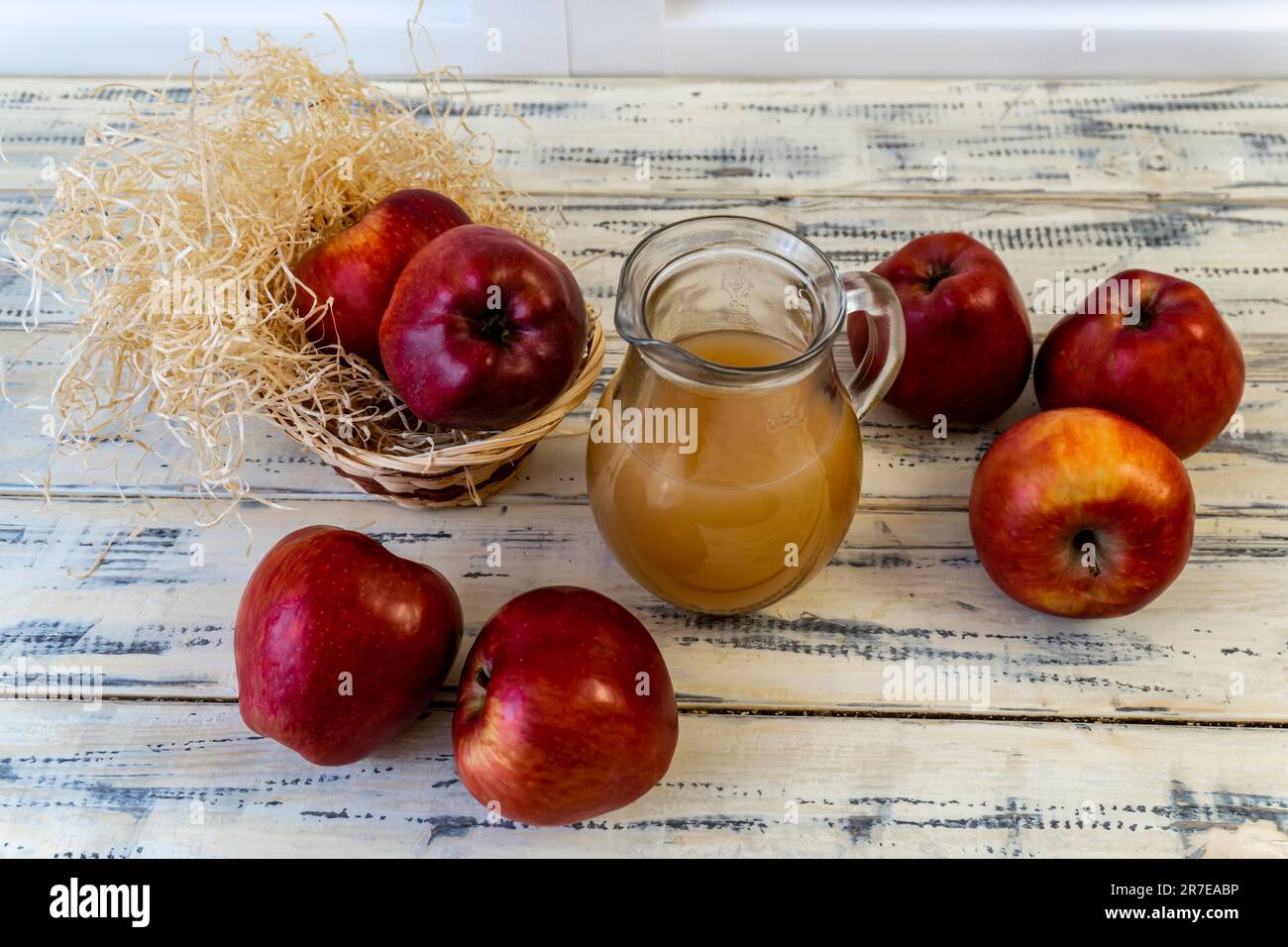 Red apples in a basket and apple juice in a jug on a wooden table Stock Photo