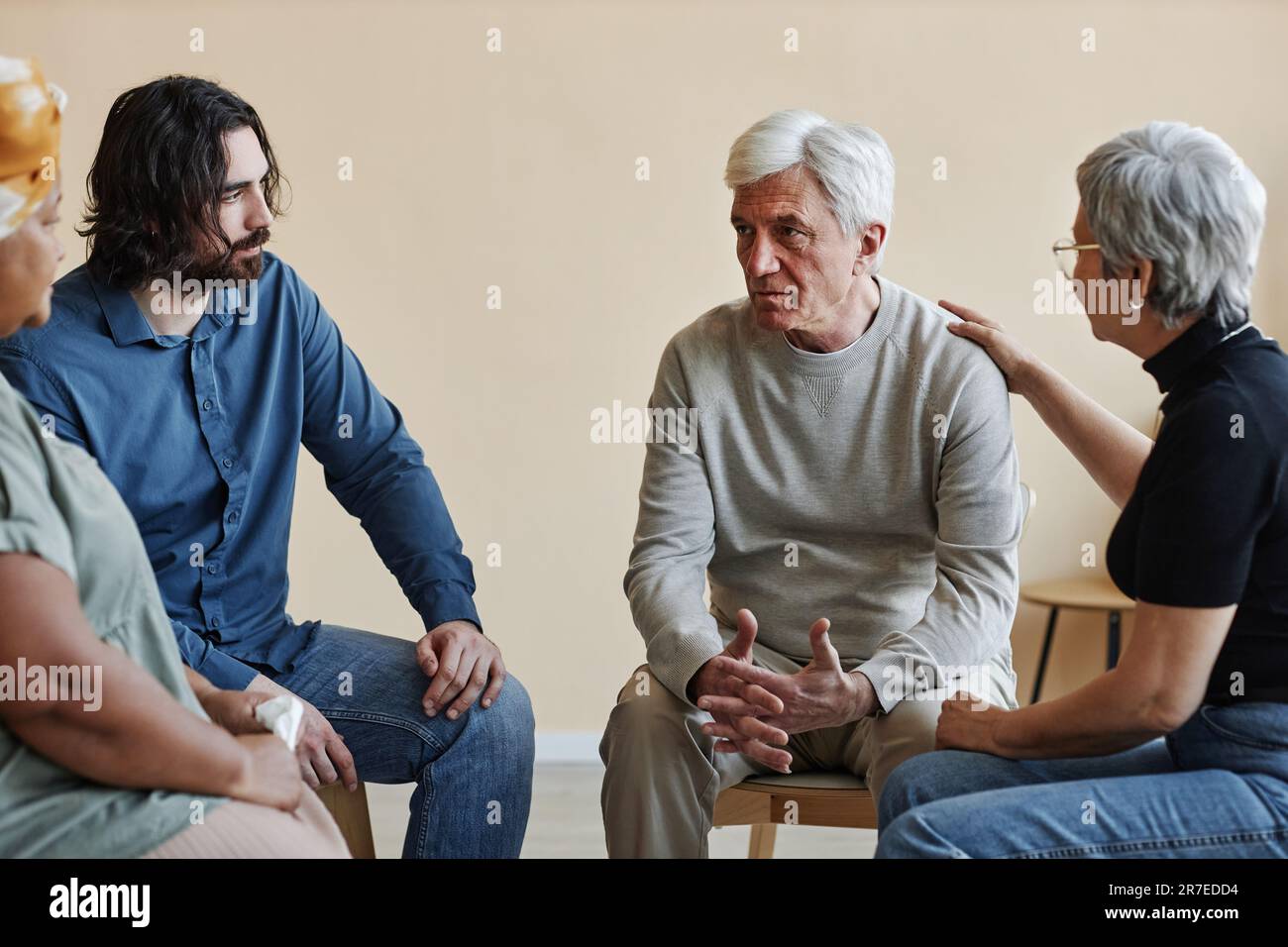 Group of senior people sitting in circle at mental health support group with white haired man