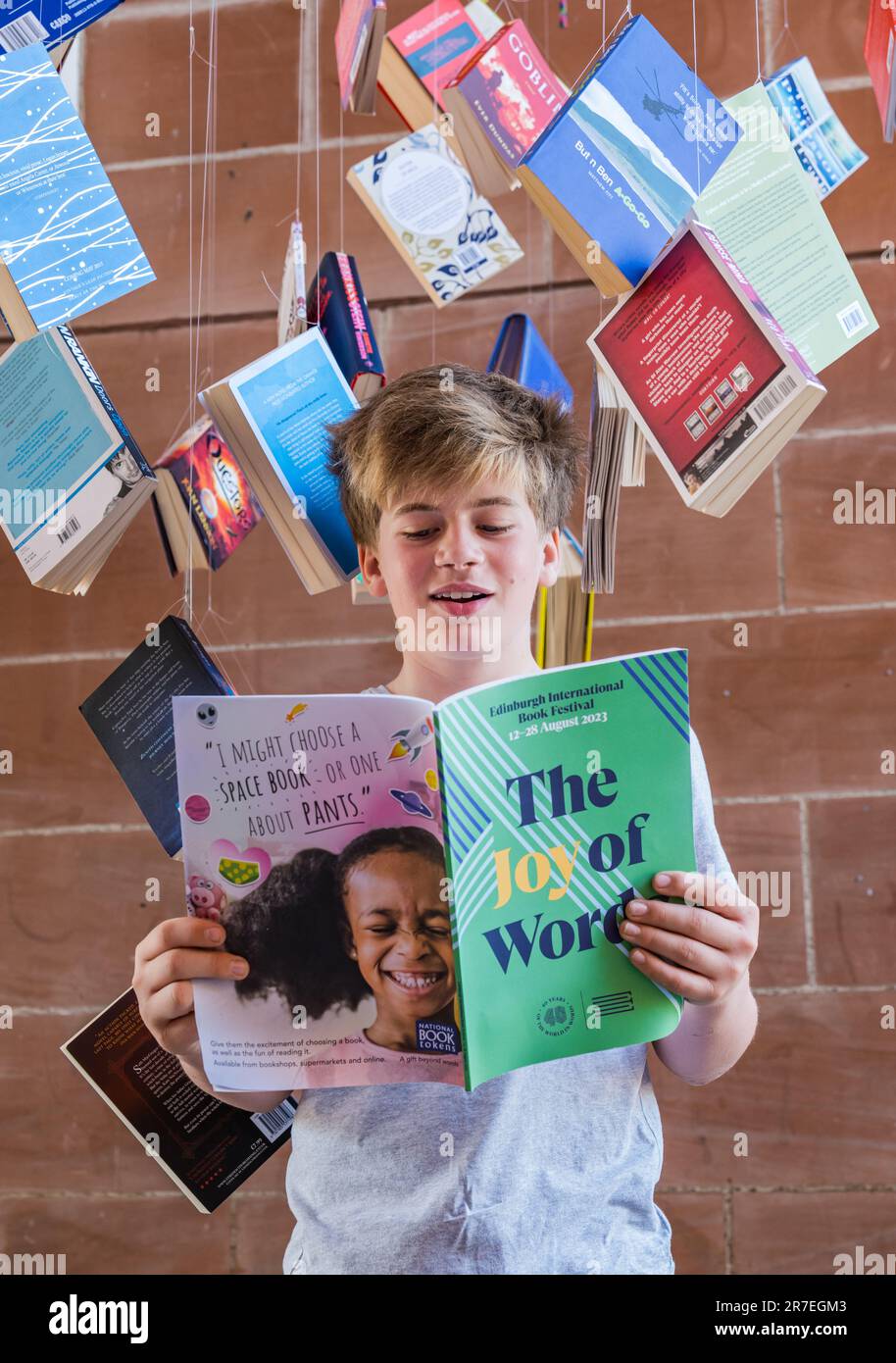 A 12 year old boy reads the Edinburgh International Book Festival 2023 programme surrounded by paperback books for programme launch, Scotland, UK Stock Photo