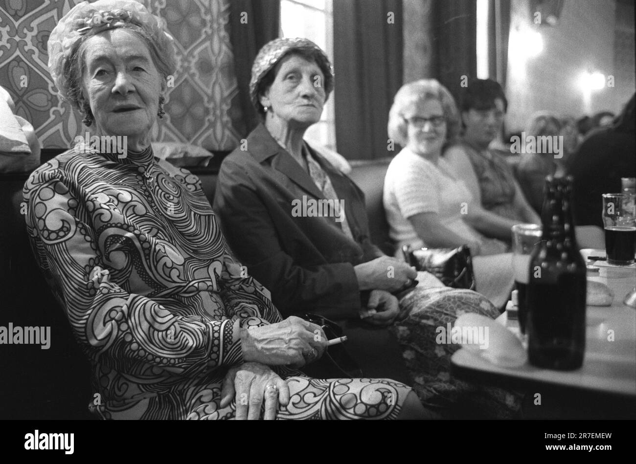 Byker Working Mens Club, Saturday evening, two older senior ladies in their best clothes, patterned dress and hats. Drinking a bottle of stout and eating a roll. Byker and St Peters Working Men's Club, Newcastle upon Tyne, Tyne and Wear, northern England circa 1973. 1970S UK HOMER SYKES Stock Photo