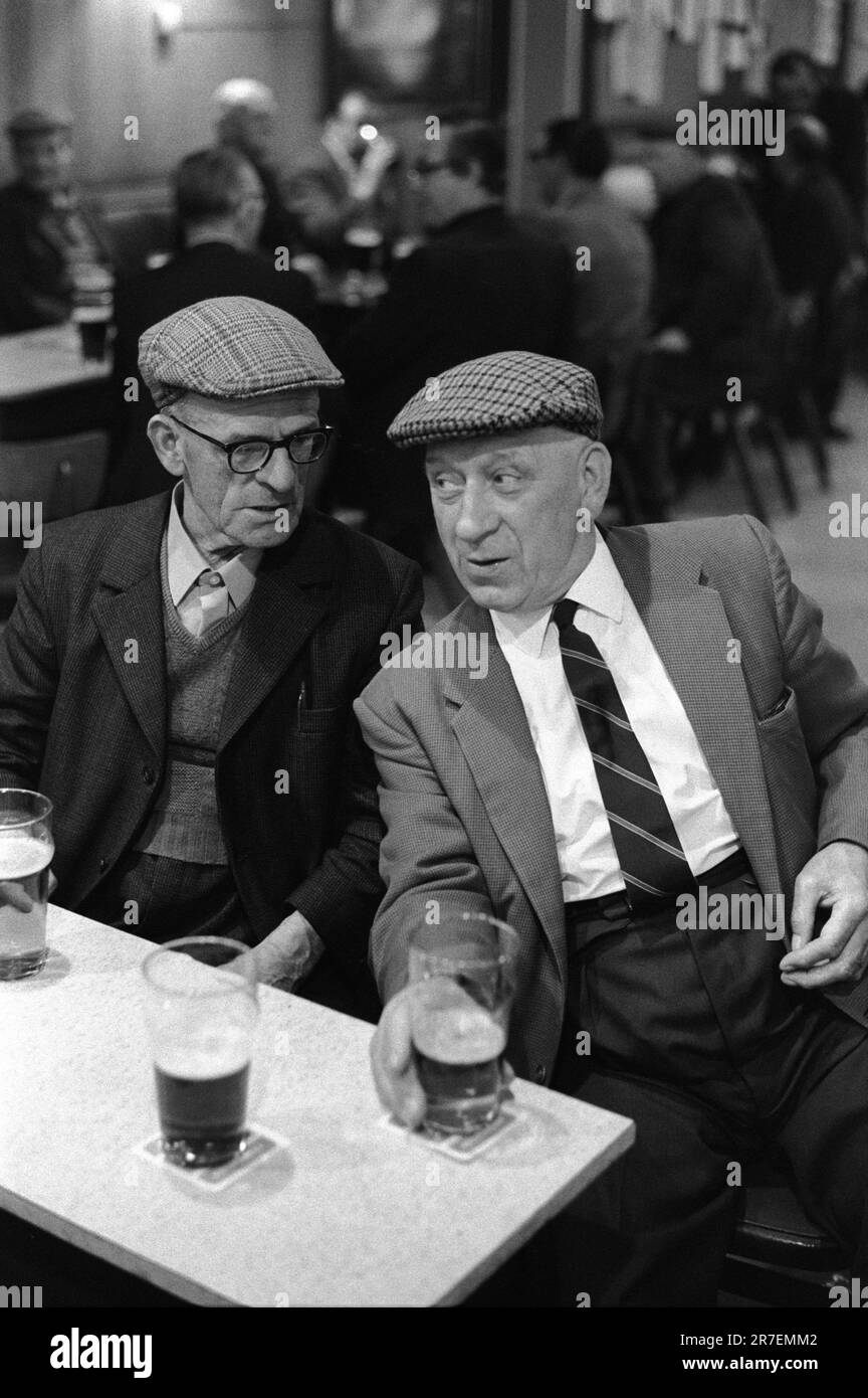 Byker and St Peters Working Men's Club, Newcastle upon Tyne, Tyne and Wear,  northern England 1973.  Saturday night and two smartly dressed men friends chat together over a pint of beer, both men are wearing flat tweed cloth caps, typical of the period. 1970S UK HOMER SYKES Stock Photo