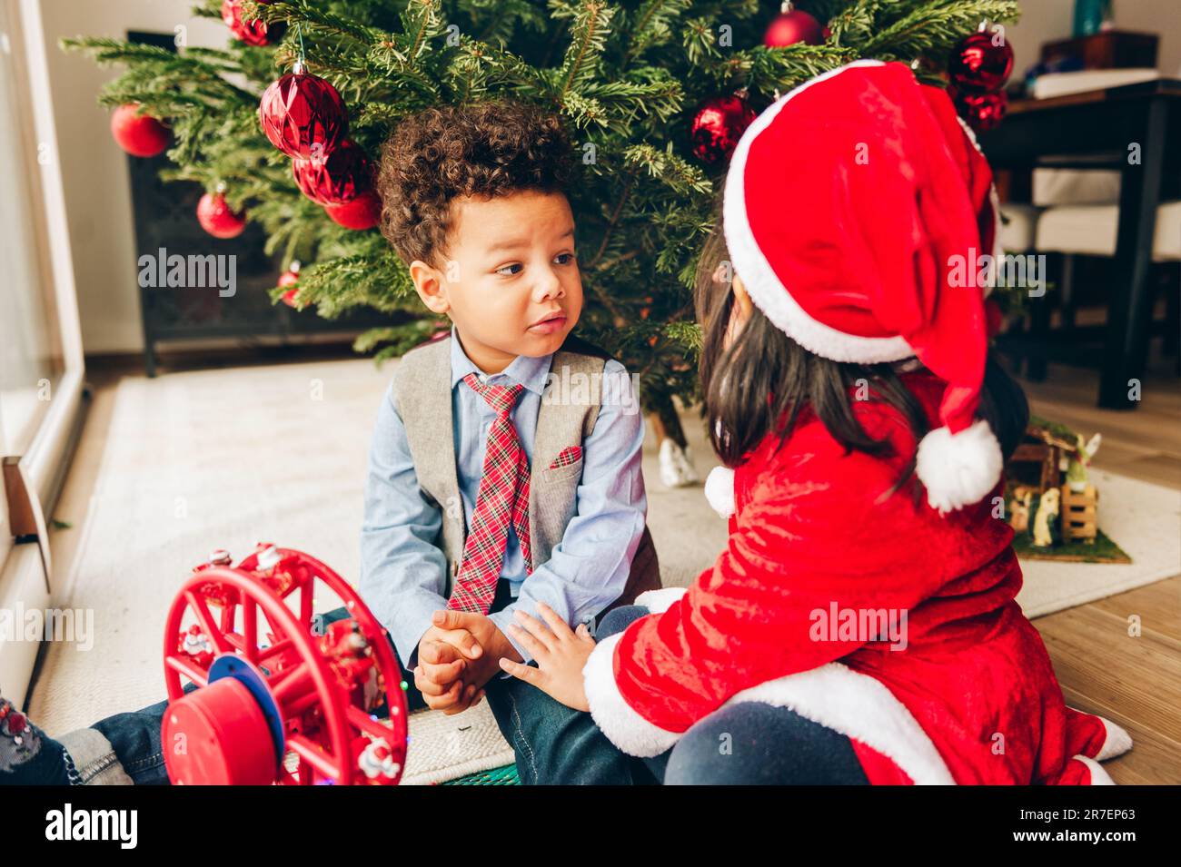 Group of two adorable 3 year old kids playing by the Christmas tree ...