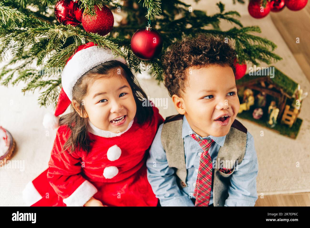 Group of two adorable 3 year old kids playing by the Christmas tree ...