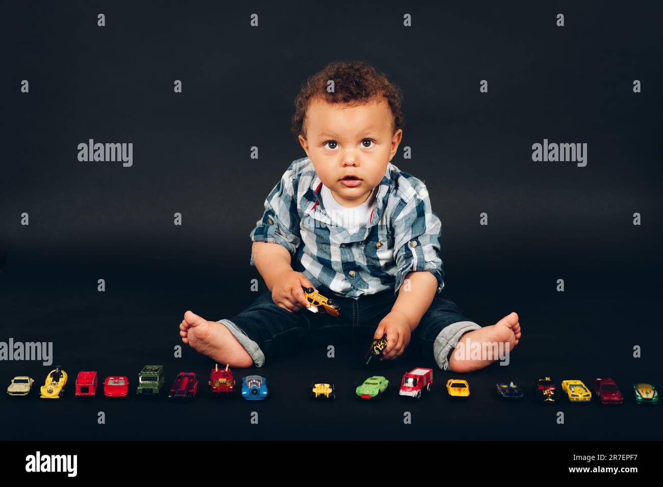 Studio shot of adorable african 9-12 month old baby boy playing with colorful mini cars Stock Photo