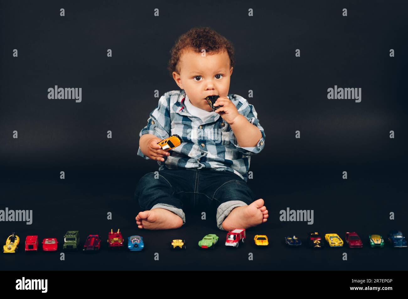 Studio shot of adorable african 9-12 month old baby boy playing with colorful mini cars Stock Photo