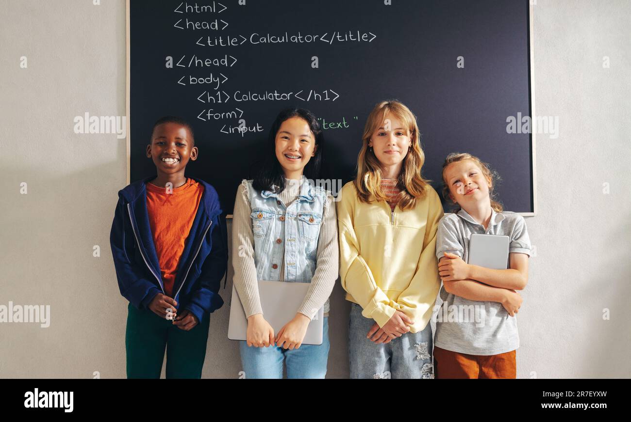 Students with diverse backgrounds stand together in a coding classroom, attending a programming lesson in a computer-based learning school. Happy elem Stock Photo