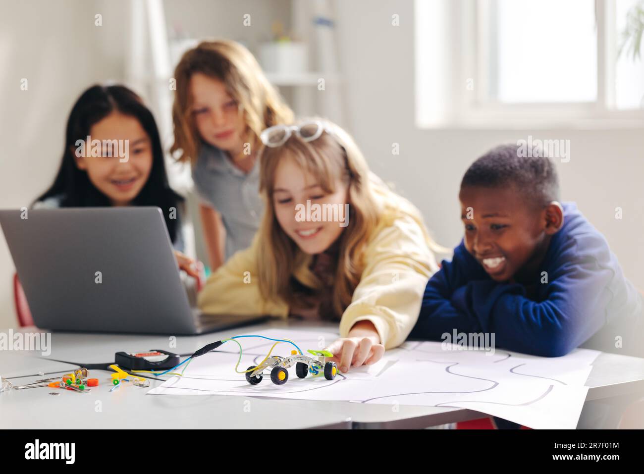 Hands-on robot programming lesson for children in a STEM classroom. Kids use education software on a laptop to program and operate robotic cars, explo Stock Photo