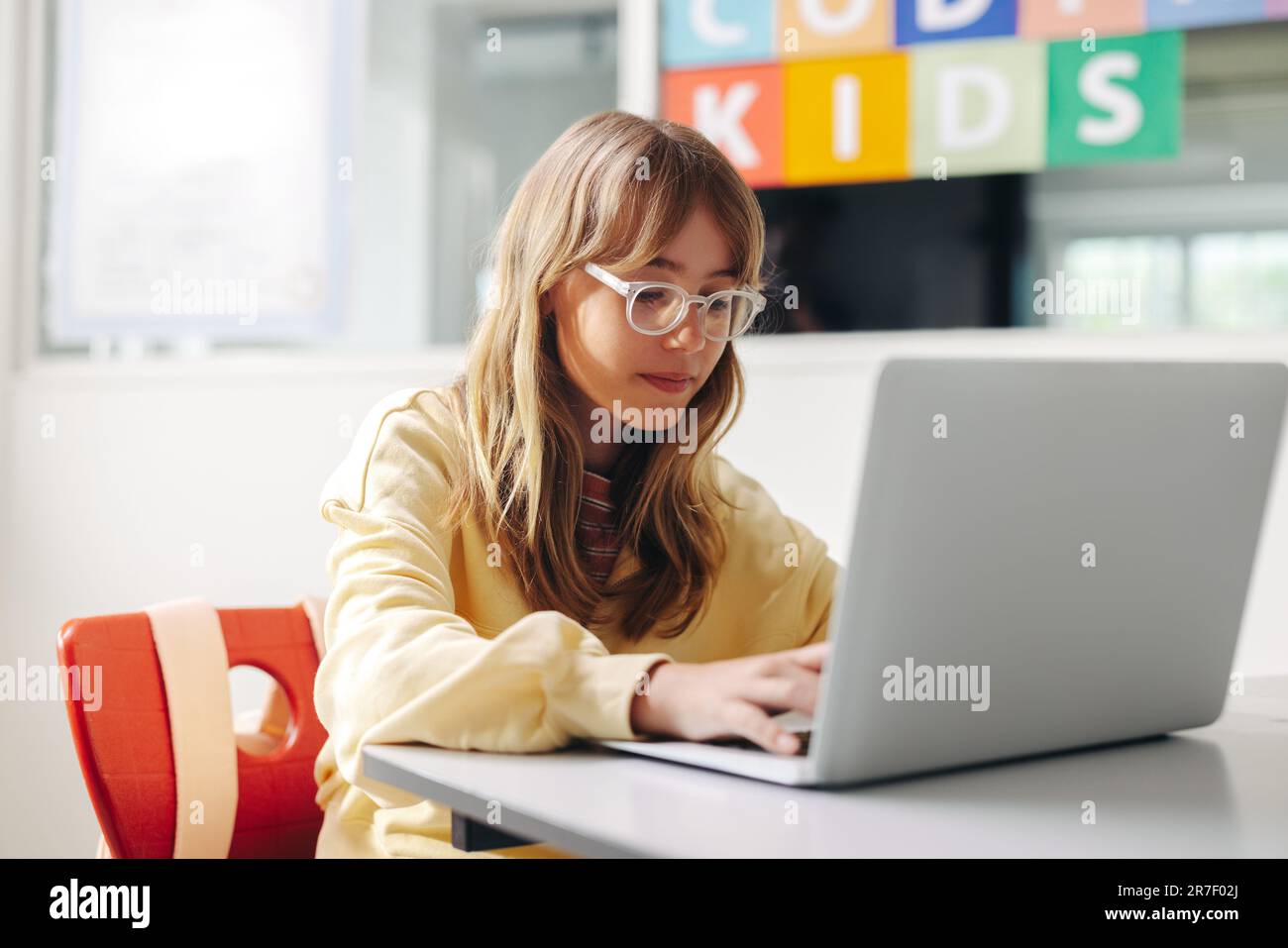 Young girl sitting in a coding classroom, using a laptop to practice programming exercises and develop her innovative skills. Female student learning Stock Photo