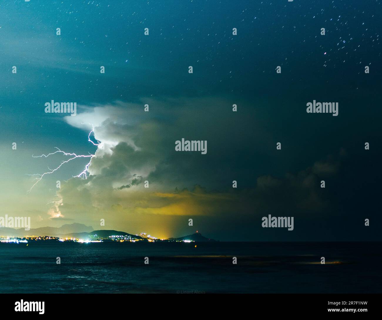 A spectacular sight of a lightning bolt descending from the sky and striking the ocean with the backdrop of majestic mountains in the background Stock Photo