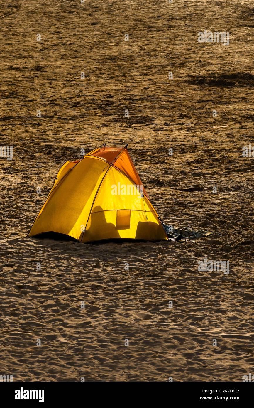 A bright yellow beach shelter backlit by evening light on Fistral Beach in Newquay in Cornwall in the UK in Europe Stock Photo