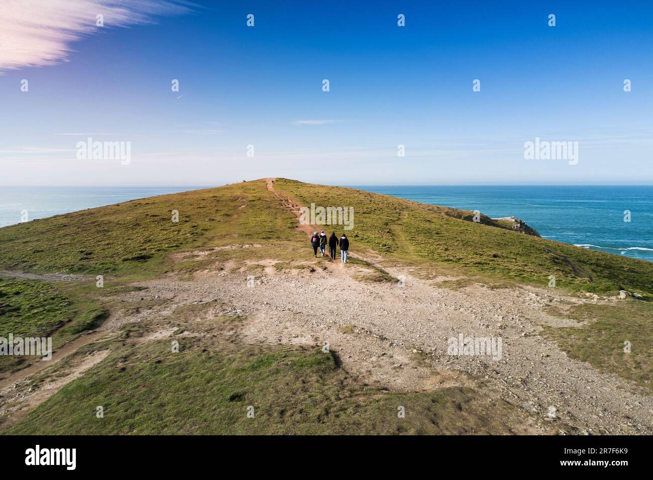 An aerial view of people walking along the worn and eroded footpath leading up to the historic round Barrow on the summit of Pentire Point East on the Stock Photo