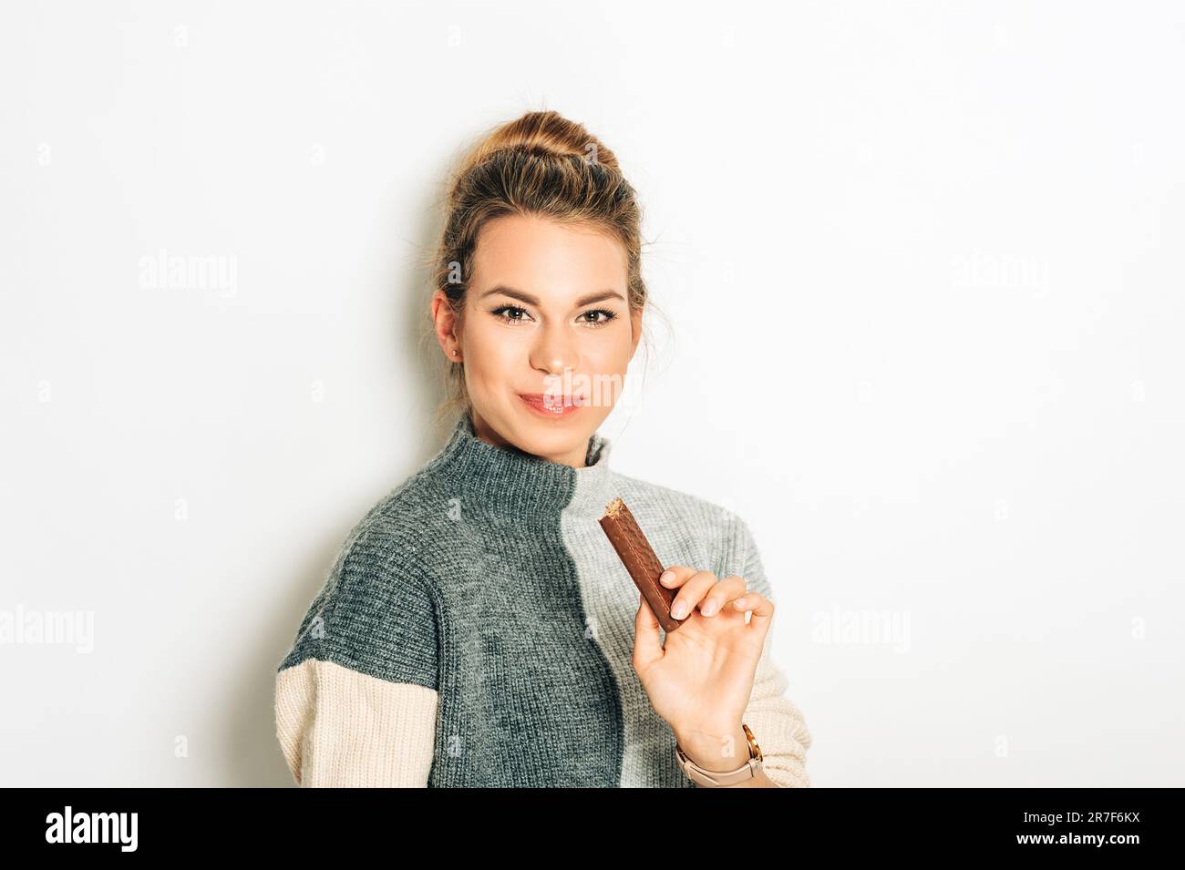 Pretty young woman eating chocolate bar, studio image taken on white background Stock Photo