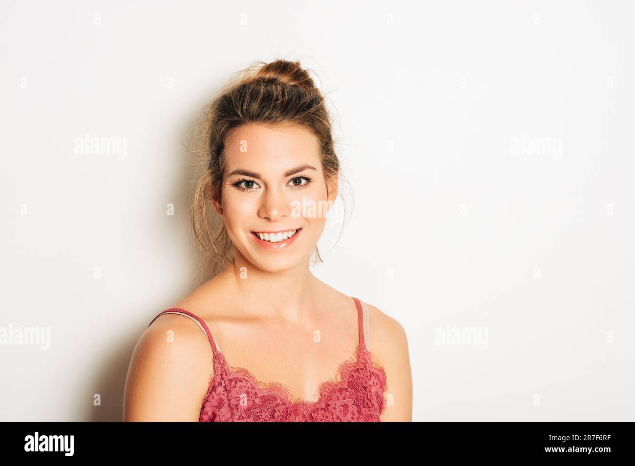 Studio shot of beautiful young woman with blond hair, chignon bun, wearing pink cami top , posing on white background Stock Photo