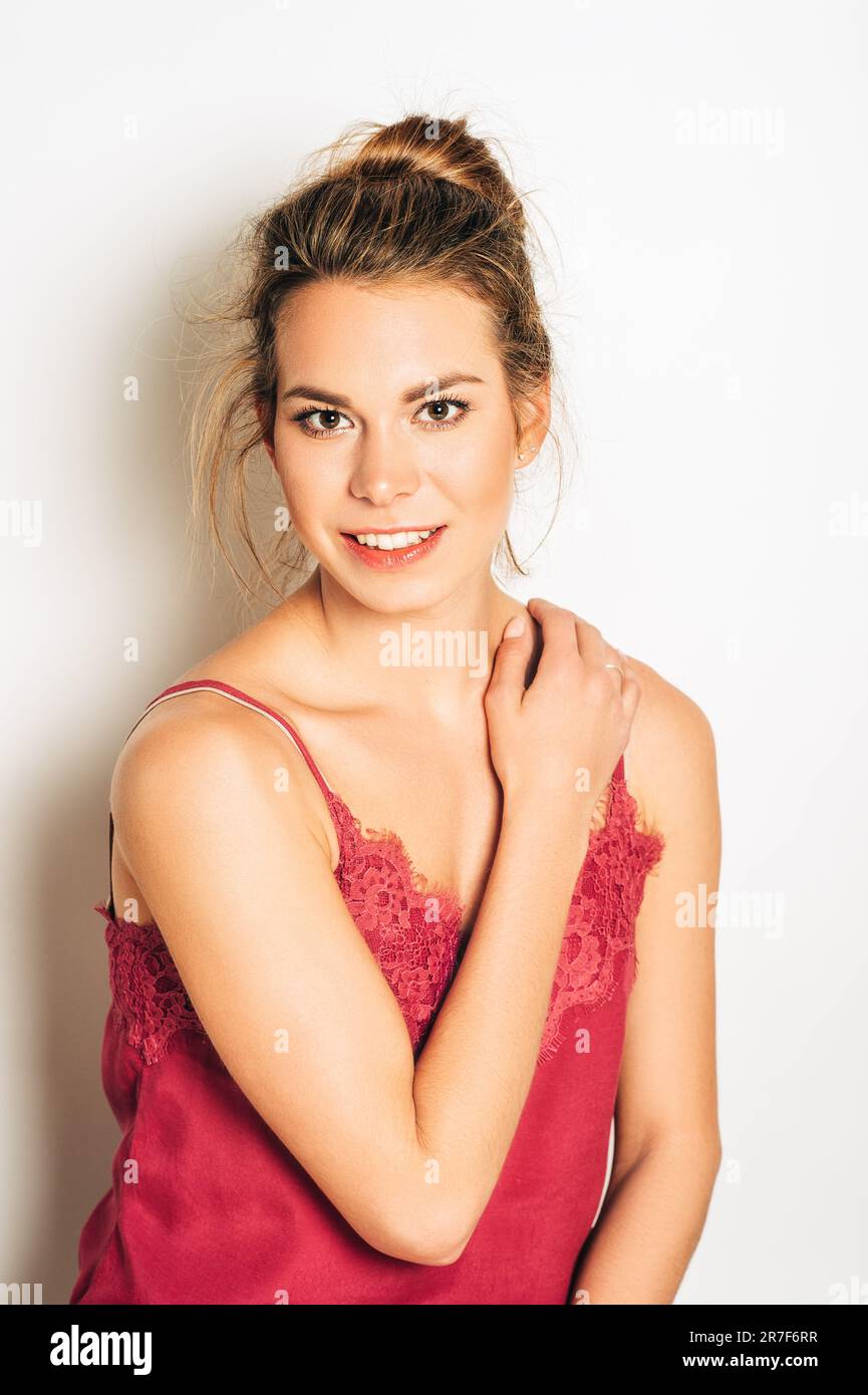 Studio shot of beautiful young woman with blond hair, chignon bun, wearing pink cami top , posing on white background Stock Photo