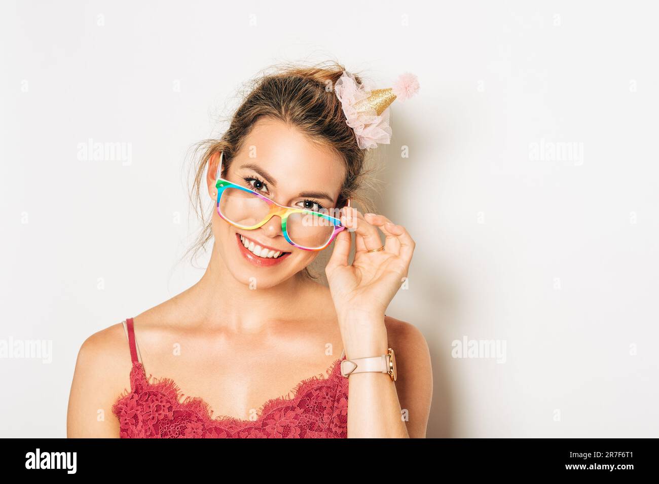 Studio shot of beautiful young woman with blond hair, chignon bun, wearing pink cami top, colorful glasses, posing on white background Stock Photo