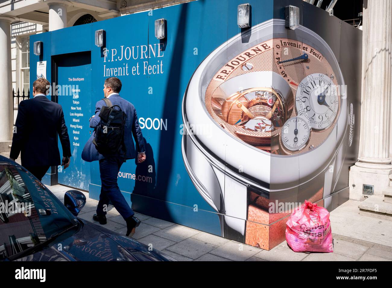 Pedestrians walk past a temporary construction hoarding for the new premises of horologist and watch manufacturer, FP Journe, in Mayfair on 15th June 2023, in London, England. The watch-maker's Latin brand identity is 'Invenit et Fecit', meaning 'invented and made'. Stock Photo
