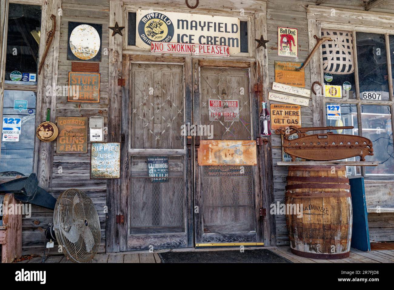 An old country general store front entryway surrounded by vintage items on the porch and rusty antique signs on the building and doors closeup view Stock Photo