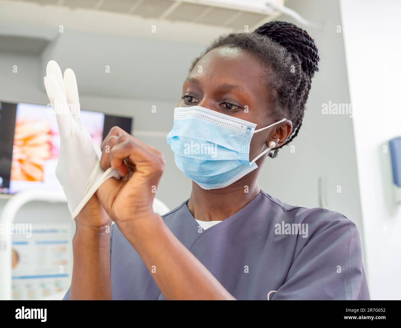 Young female dentist with a mask on putting on her gloves in a dental