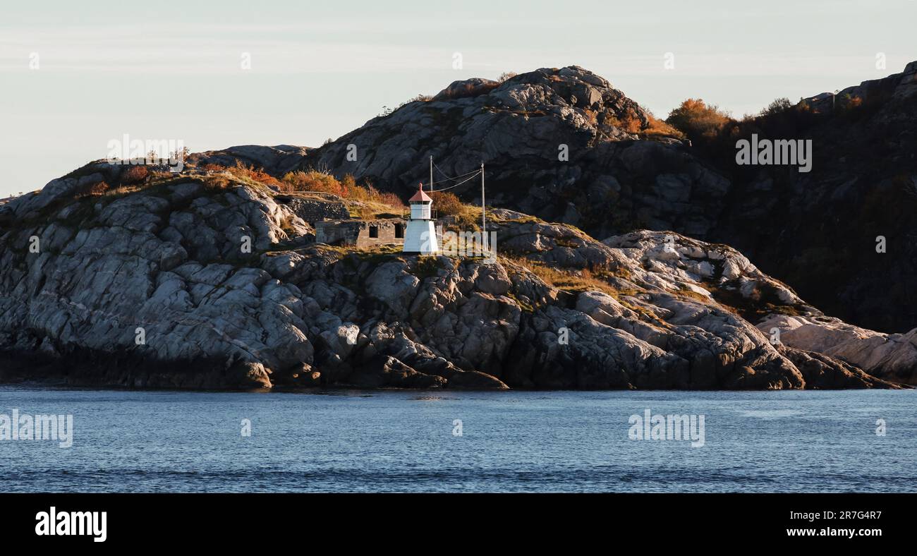 White lighthouse tower with red top stands on dark coastal rocks ...
