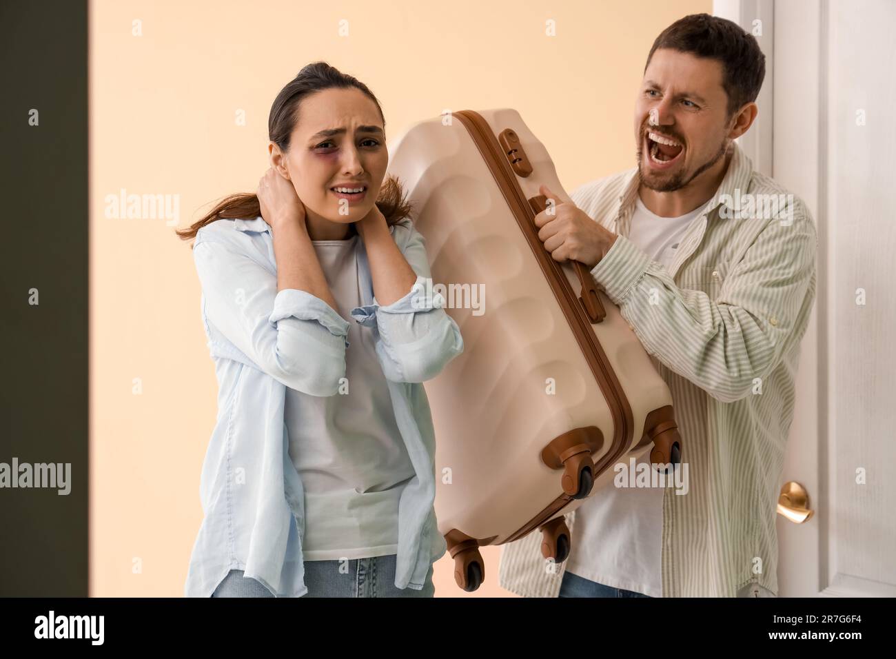 Angry husband kicking his wife with suitcase out near door. Domestic violence concept Stock