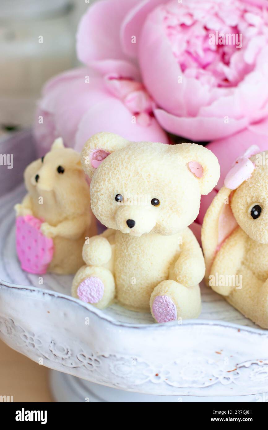 Cute edible teddy bear, bunny and hamster toys made of white chocolate with fresh peonies and candles on the backgrounds. Gift for a baby Stock Photo