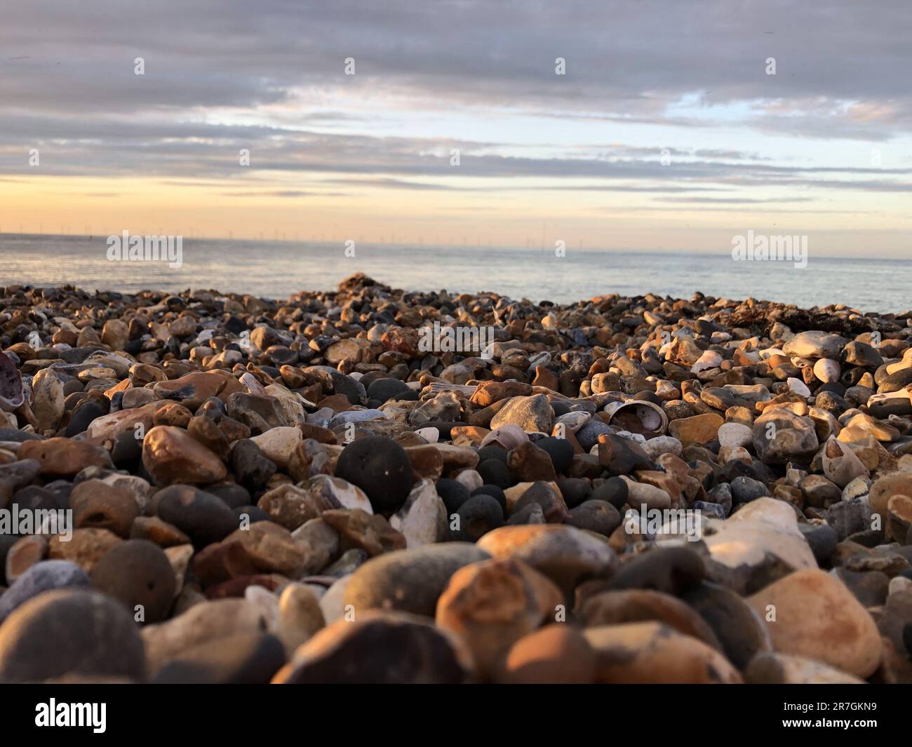 Western esplanade stone beach, colourful pebbles at the beach. Looking across the north sea at the wind turbines. In Herne Bay, Kent, UK. Stock Photo