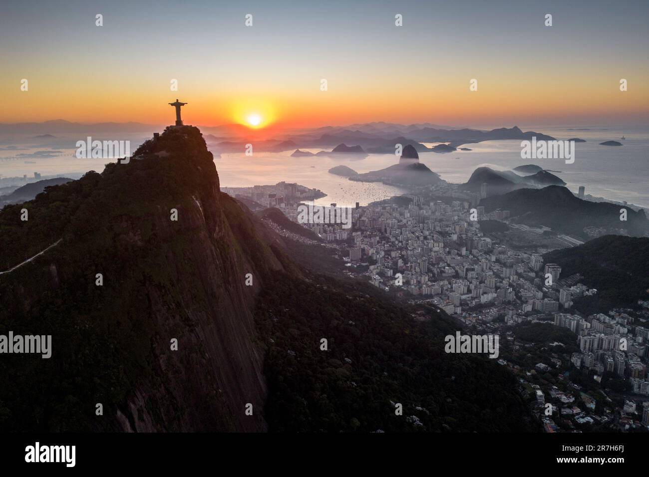 Rio de Janeiro, Brazil - June 10, 2023: Christ the Redeemer statue on top of Corcovado Mountain with the Sugarloaf Mountain in the horizon on sunrise. Stock Photo