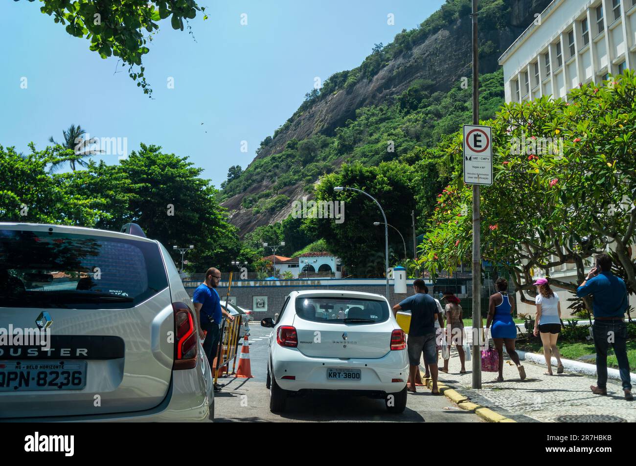 Cars and tourists arriving at General Tiburcio square parking area nearby Praia Vermelha beach in Urca district under summer morning sunny blue sky. Stock Photo