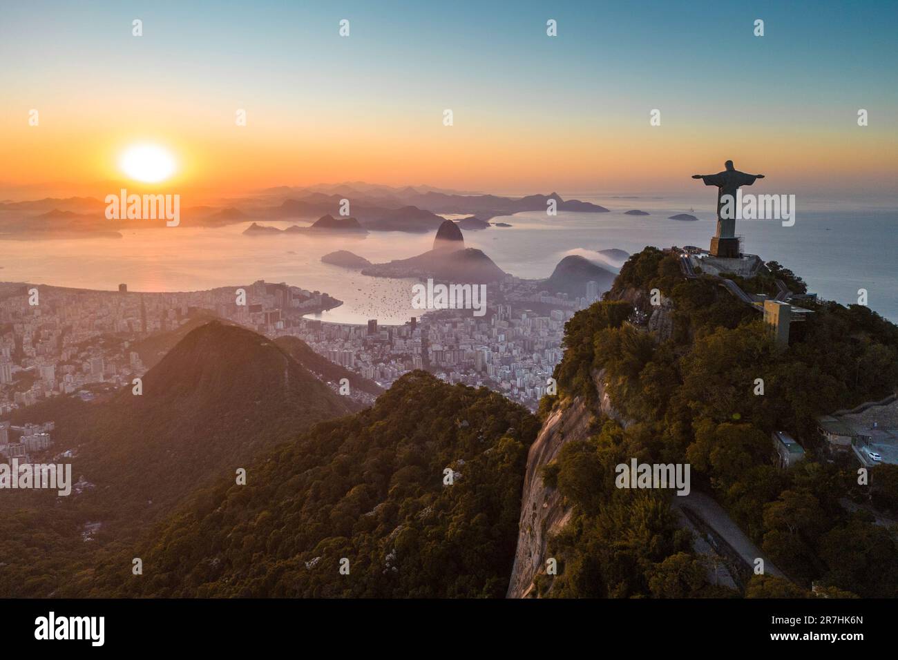 Rio de Janeiro, Brazil - June 10, 2023: Christ the Redeemer statue on top of Corcovado Mountain with the Sugarloaf Mountain in the horizon on sunrise. Stock Photo