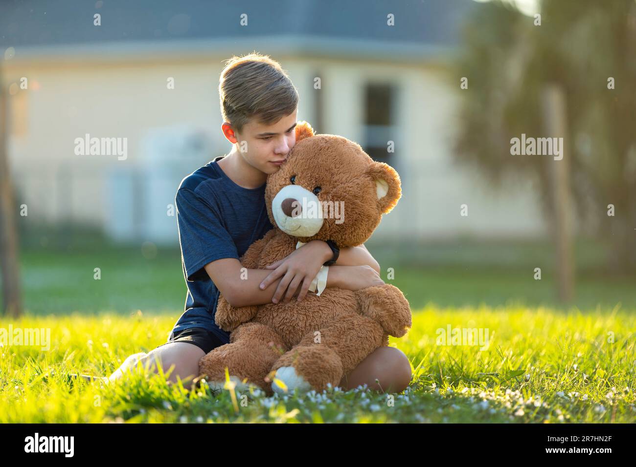Happy teenager boy hugging his teddy bear friend outdoors on green