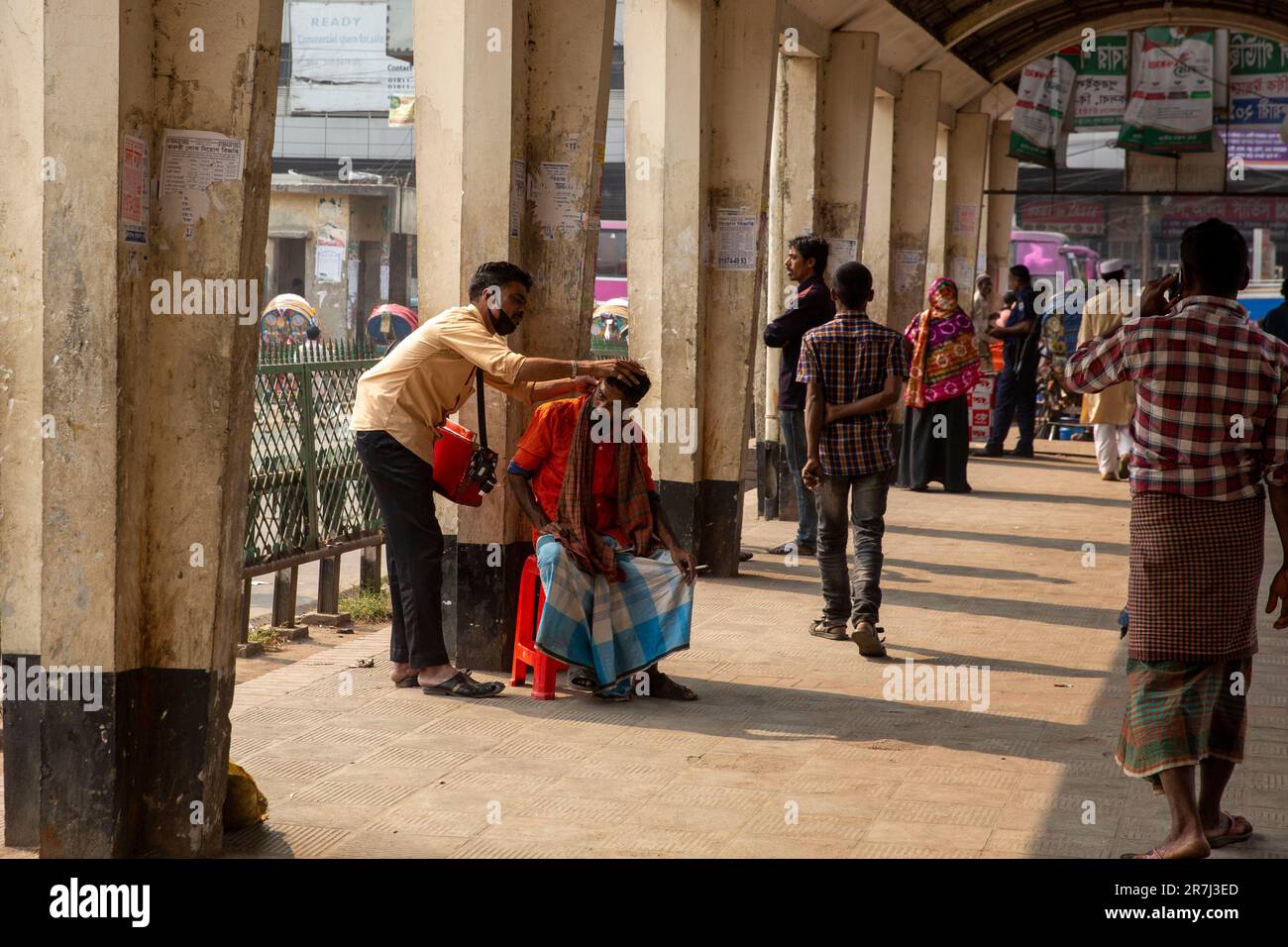 A man gets clean his ears from a street ear-cleaner at Kamlapur Railway Station in Dhaka, Bangladesh Stock Photo