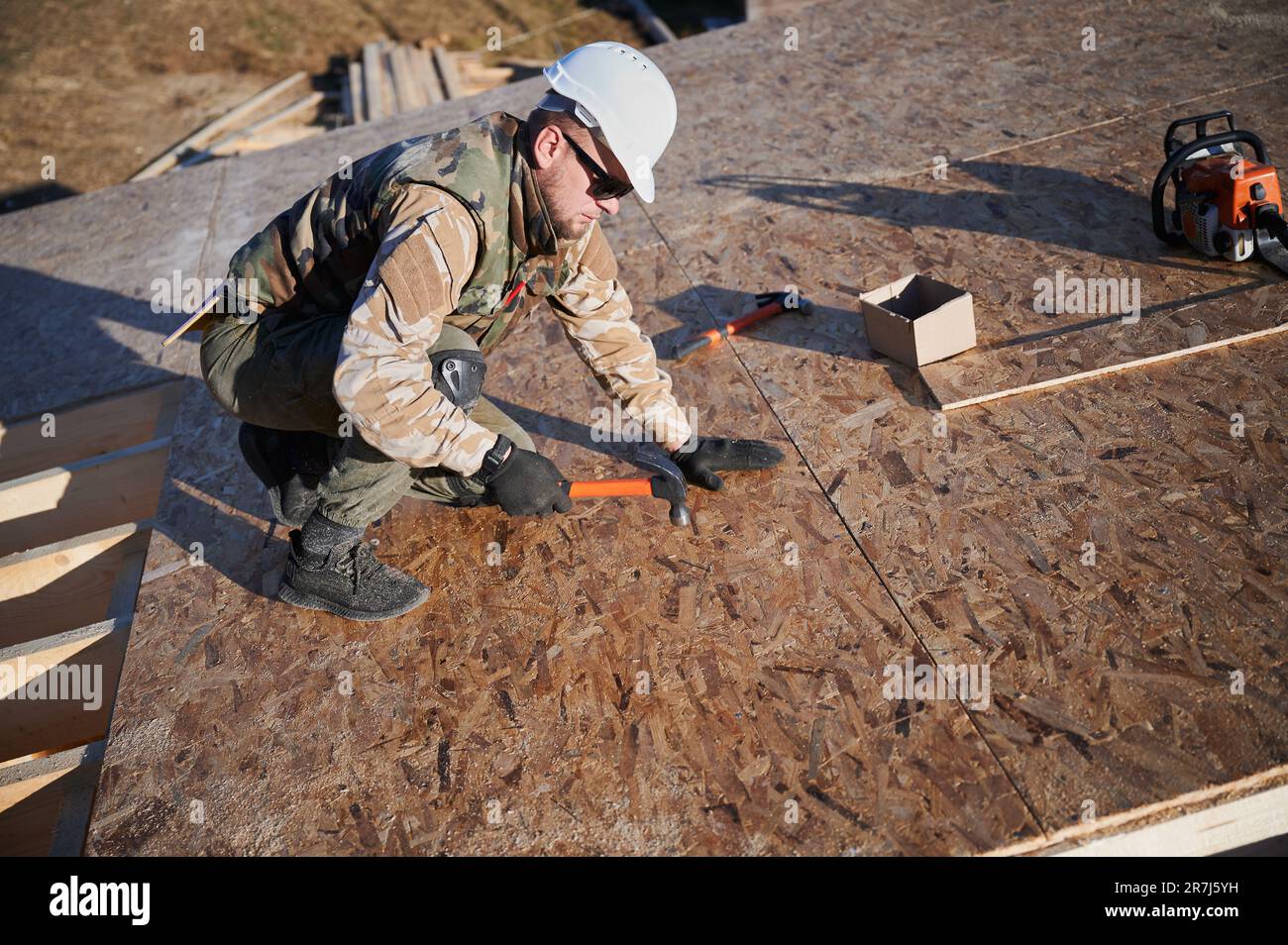 Carpenter hammering nail into OSB panel on the roof top of future