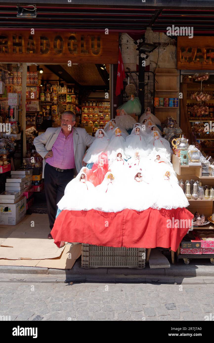 Man stands beside a table full of Dolls in wedding dresses outside a shop in the Fatih area of Istanbul, Turkey Stock Photo