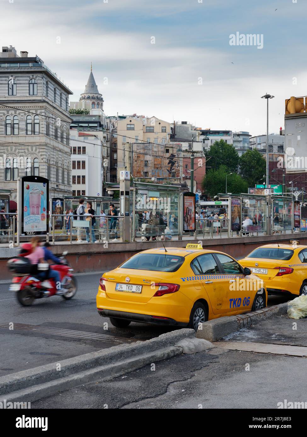 Yellow taxis on Galata Bridge as a motorbike speeds past. People wait at Karakoy Tram stop. Galata Tower in background. Istanbul, Turkey. Stock Photo