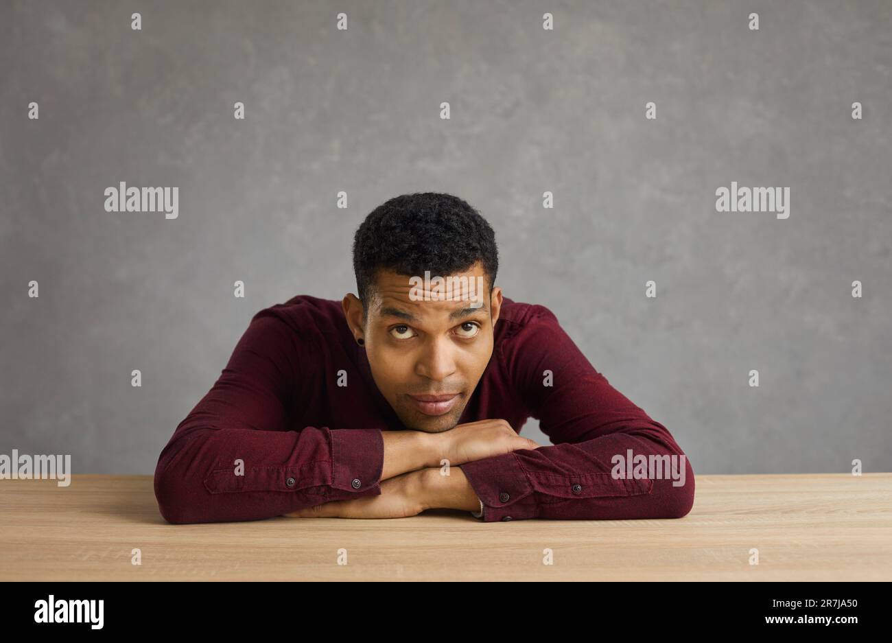 Sad thoughtful man putting head on hands sitting at desk studio portrait Stock Photo