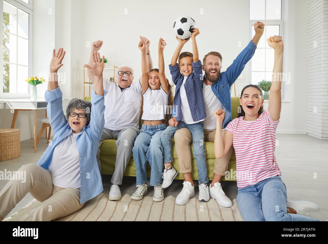 Big family watching sports match on tv at home, cheering and shouting goal with hands up. Stock Photo