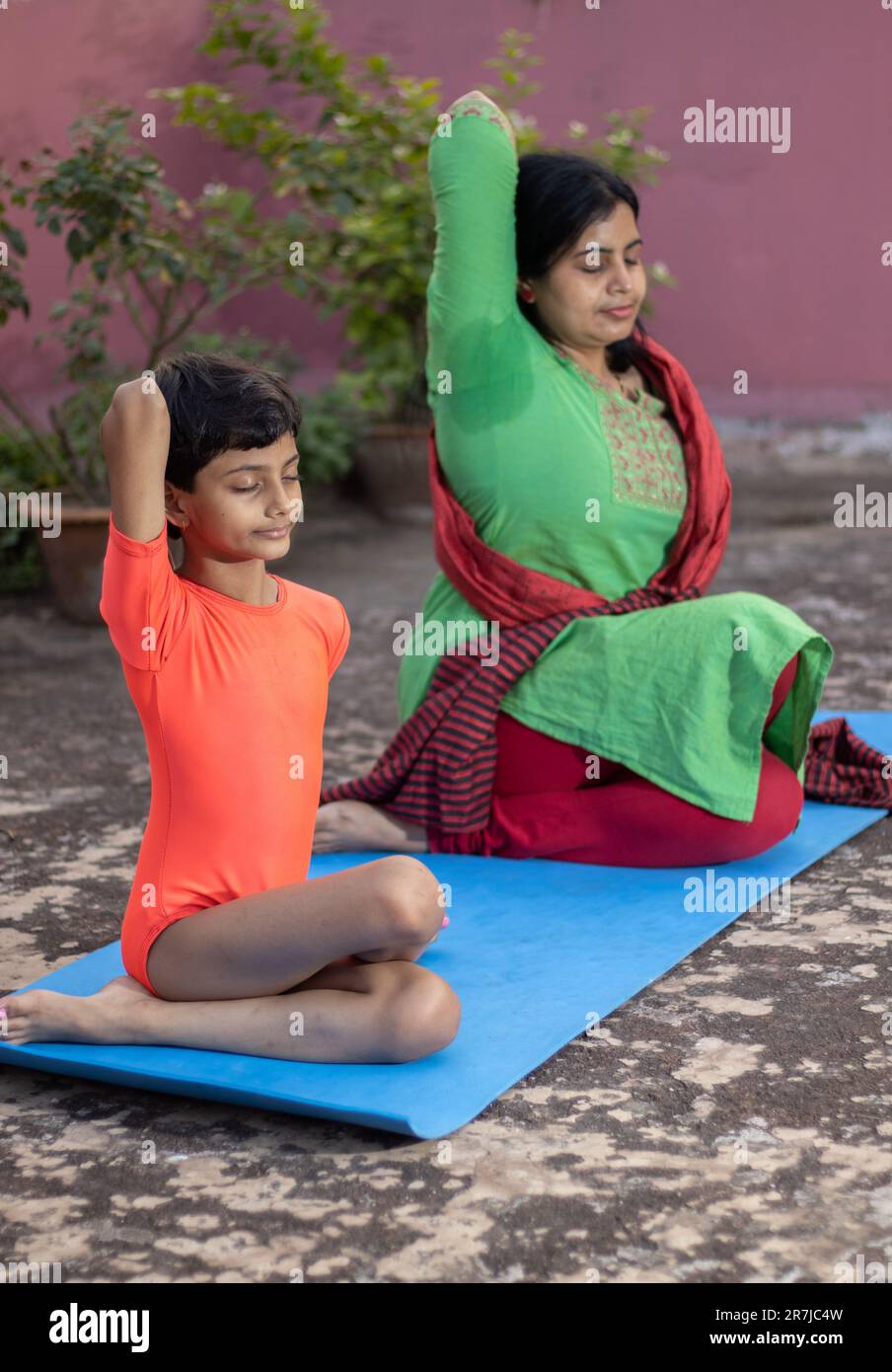 An Indian girl child and mother practicing Gomukhasana yoga on yoga mat ...