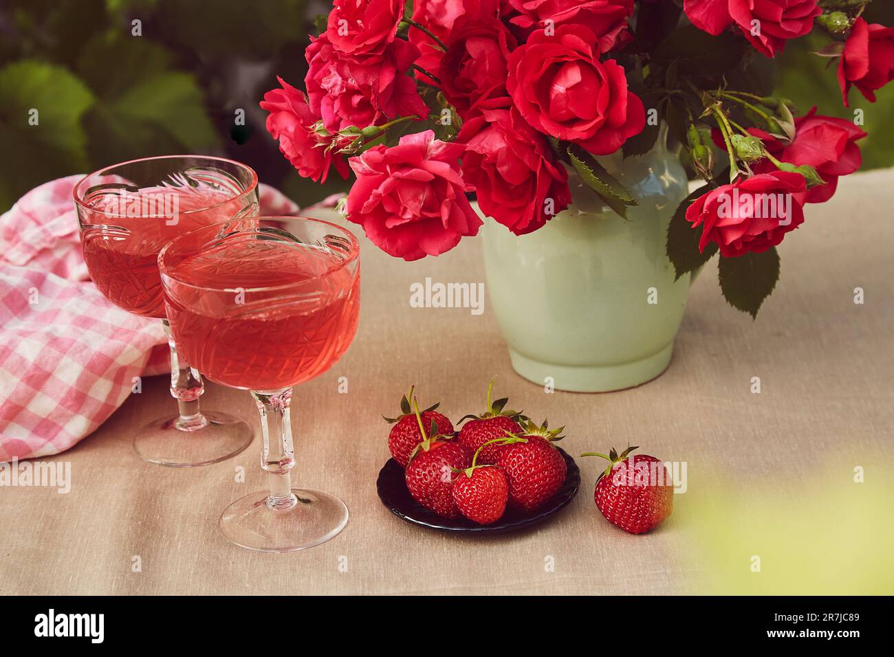 Couple glasses of red sparkling strawberry wine with roses outdoor, strawberry and chocolate. Aesthetic summer table settings Stock Photo