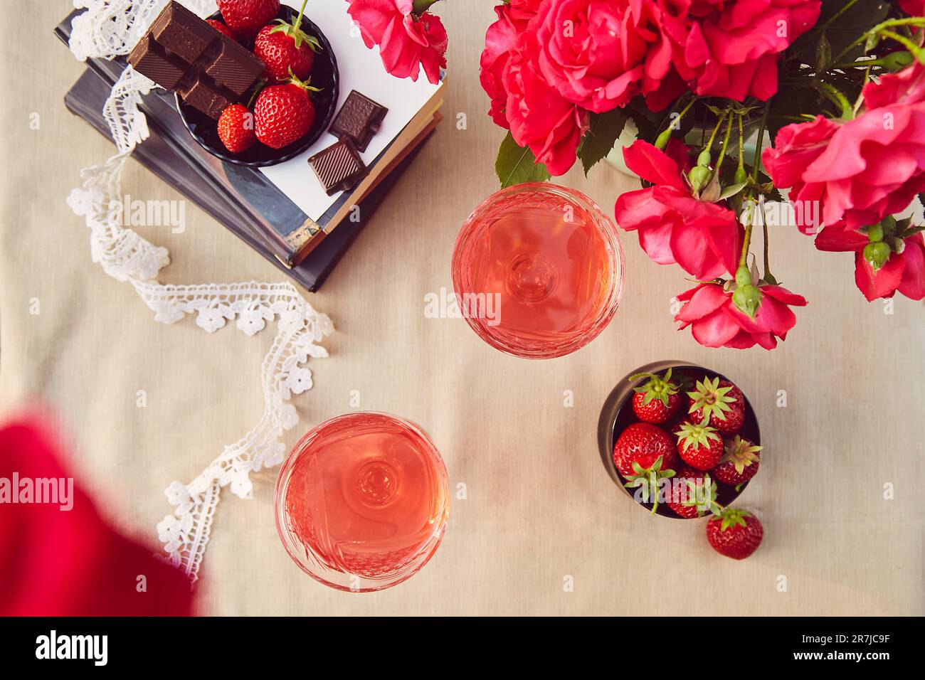 Aesthetics summer table settings. Couple of glasess with red homemade, strawberry infusion. Strawberry and chocolate. Roses bouquet. Flat lay. Stock Photo