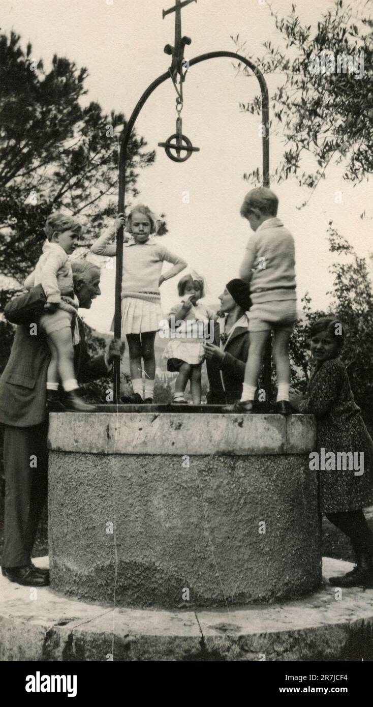 Children playing on top of a well with their relatives, Italy 1920s Stock Photo