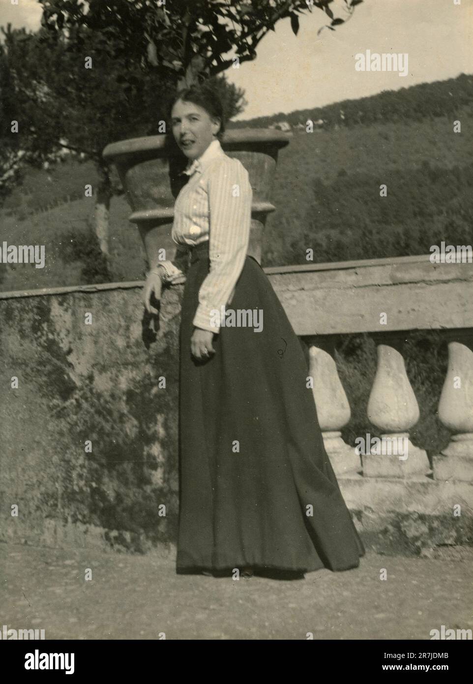 Full-lenght portrait of a woman wearing a long skirt laying on a banister outside, Italy 1900s Stock Photo