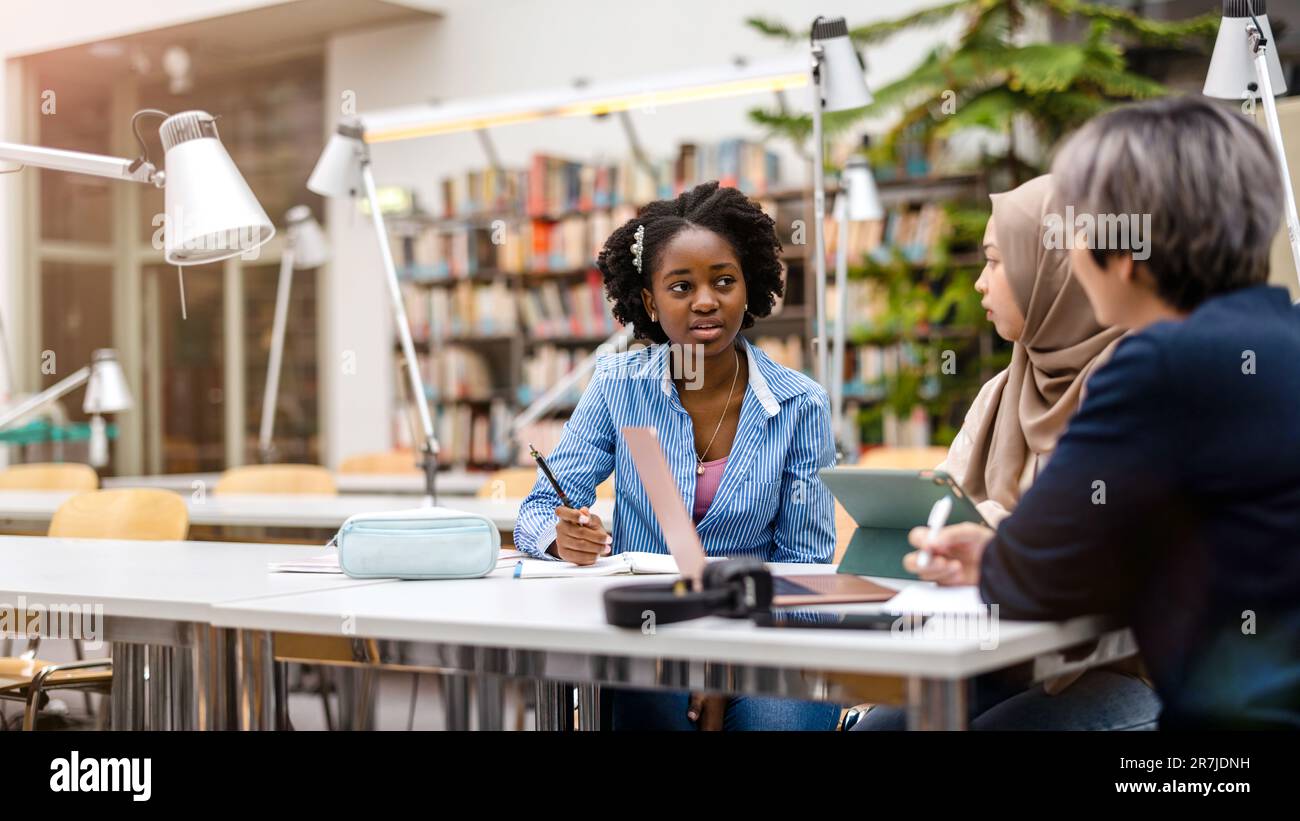 Multiethnic group of students sitting in a library and studying ...